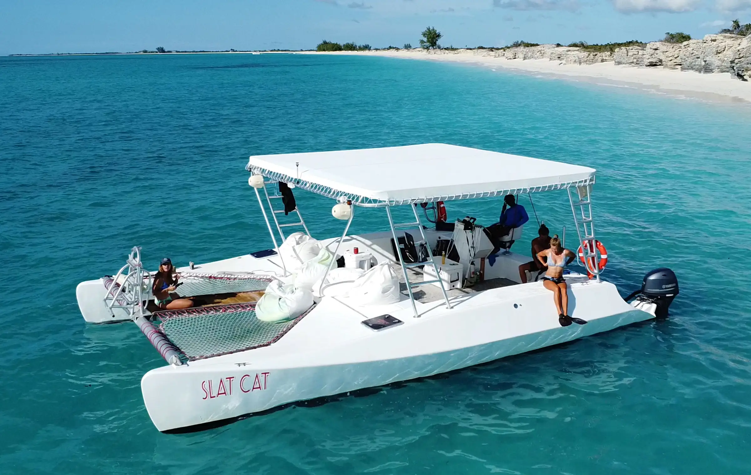 Slat Cat, a motor catamaran with a white canopy, cruising past a long white beach