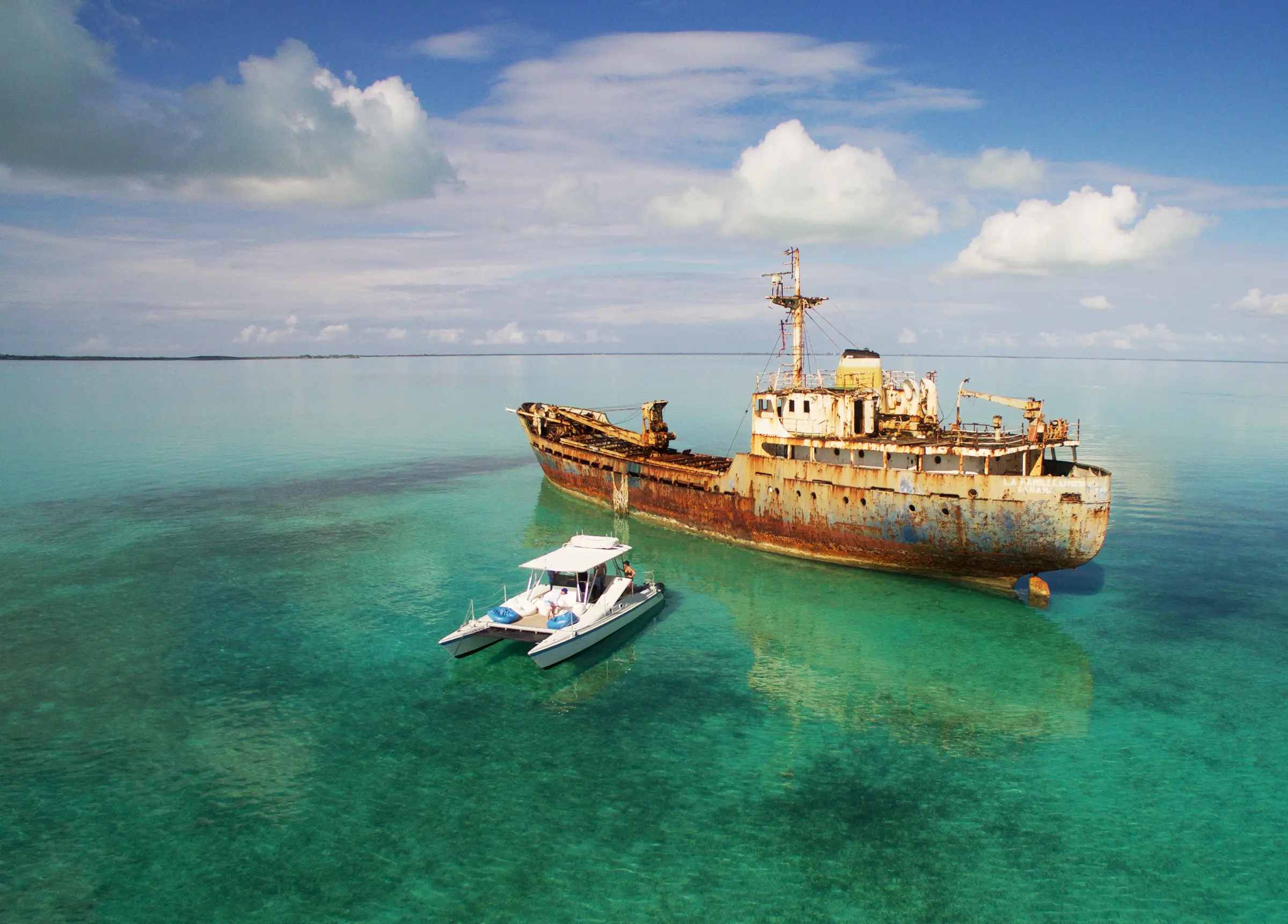 A catamaran beside a rusting shipwreck in shallow turquoise water